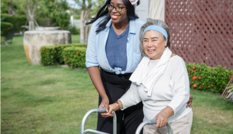 asian senior mother walk with walker and african american carer support in garden at home
